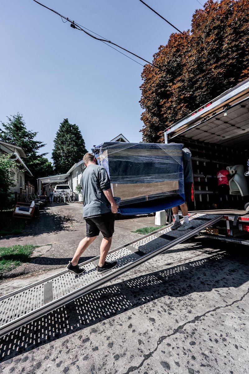Home 1 Moving Fellows crew loading a blanket-wrapped item into the moving truck at a Portland home